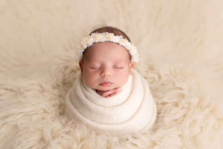 Sleeping newborn wrapped in cream on a soft fur rug