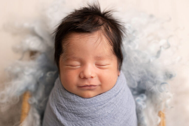 Smiling newborn swaddled in blue on a soft fluffy blanket