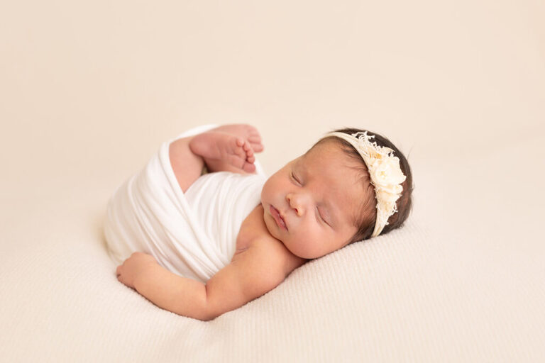 Sleeping newborn baby wrapped in cream with a floral headband at the Beaconsfield studio