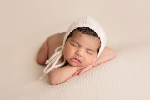 Sleeping newborn in a white knitted bonnet resting on folded hands